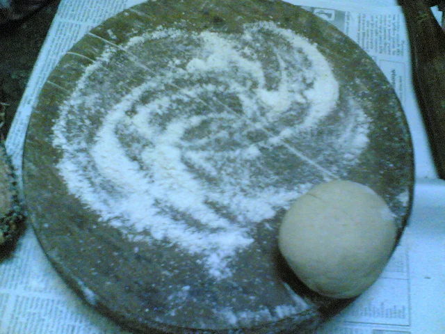 Round rolling board dusted with flour, with a dough ball at one edge