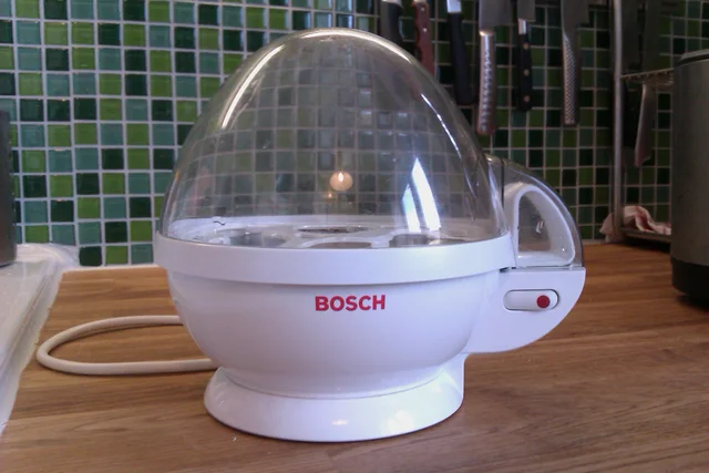 White Bosch egg boiler with a clear domed lid, visible egg tray and side switch