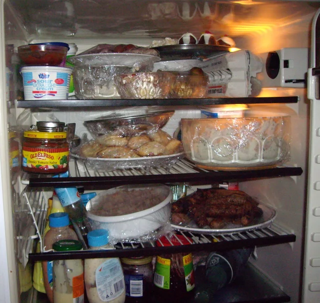 Crowded refrigerator shelves containing bowls, jars and bottles with limited access space