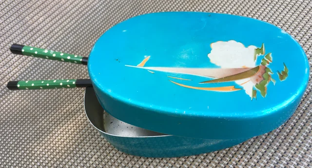 Historical blue oval bento box with a partly open decorated lid and chopsticks