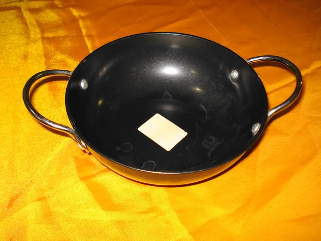 Dark deep kadai with two riveted loop handles on a yellow surface