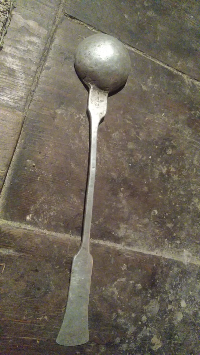 Long-handled metal ladle with a round bowl, photographed from the back