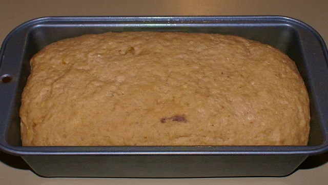 Baked loaf in a dark rectangular loaf pan with projecting end rims