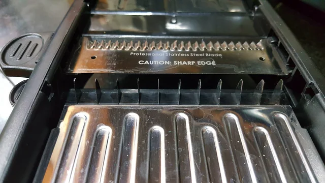 Close-up of a mandoline cutting deck with a straight blade and upright julienne blades