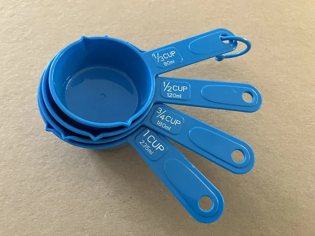 Four nested blue measuring cups with handles labelled in cup fractions and millilitres