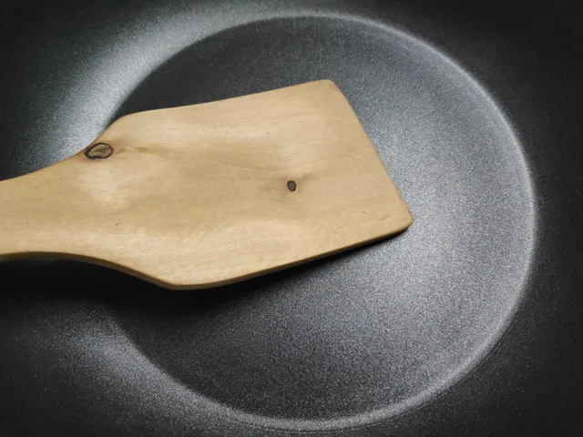 Wooden spatula across the dark speckled interior of a pan