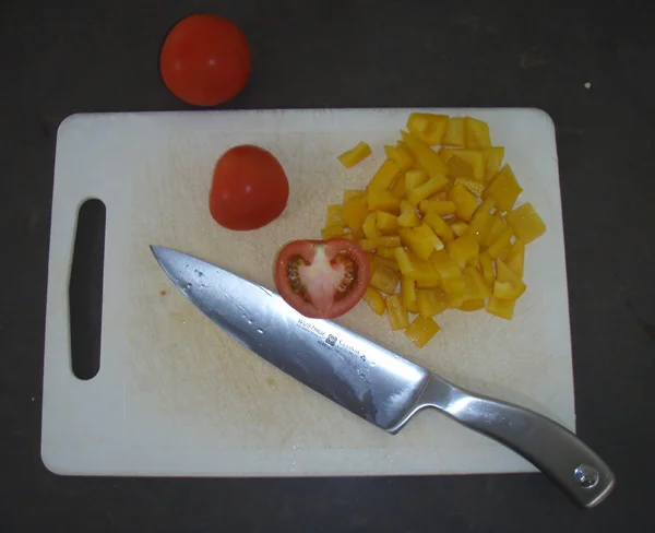 White plastic cutting board with tomato, chopped yellow pepper and a knife
