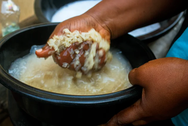 Hands washing rice in water in a dark bowl