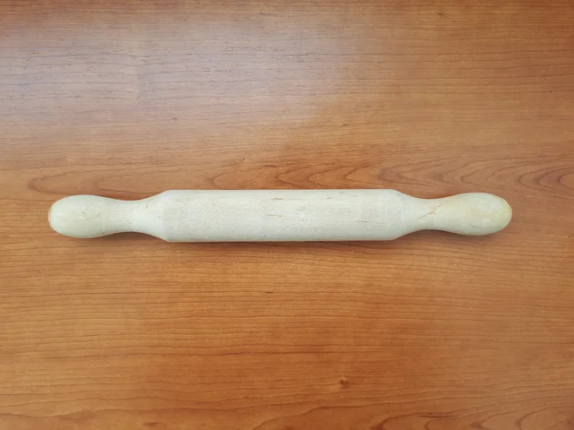 Wooden rolling pin with narrowed grip ends lying on a wooden surface