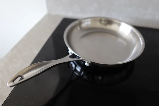 Empty stainless-steel frying pan with a long handle on a dark cooktop
