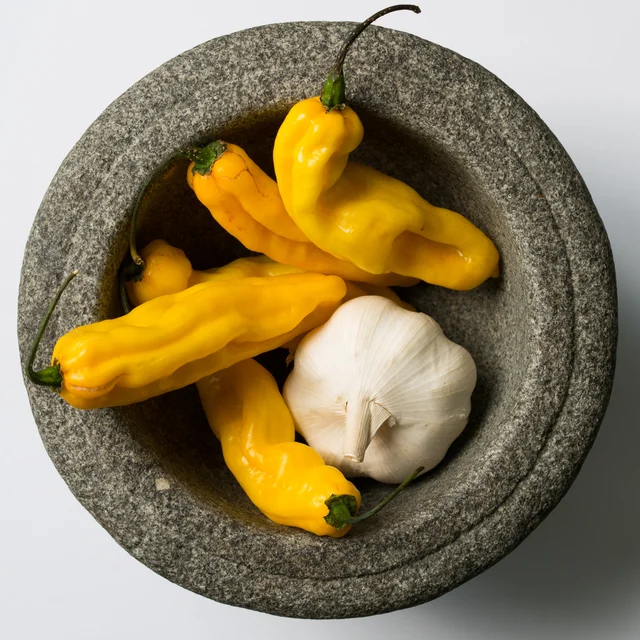 Stone mortar containing yellow peppers and a whole garlic bulb, viewed from above