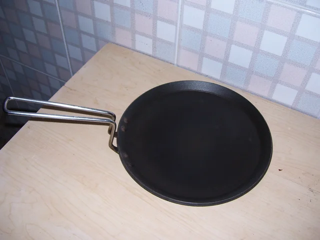 Dark round tawa with an attached double-rod metal handle on a wooden surface