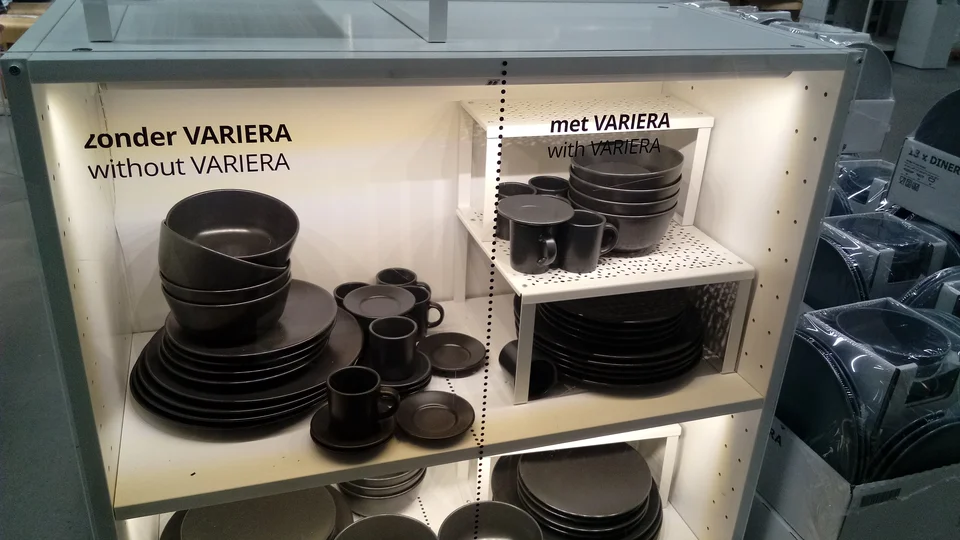 White VARIERA shelf inserts separate bowls, plates and cups in an IKEA store cupboard display
