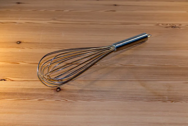 Metal balloon whisk lying diagonally on a wooden table